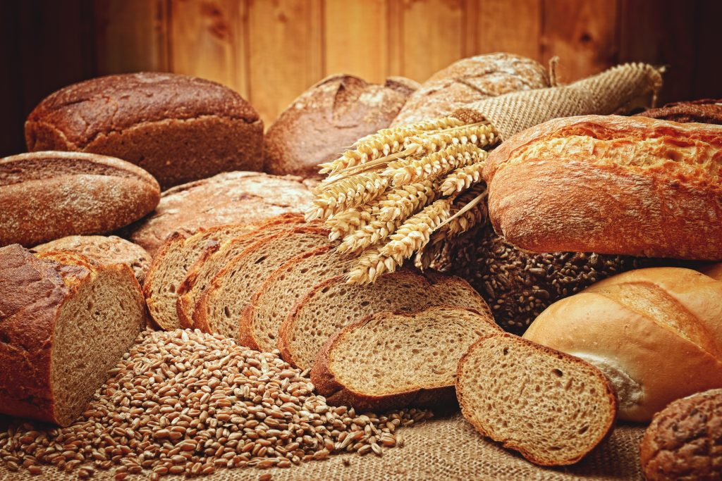 A variety of bread loaves, sliced bread and grain on a burlap sack.